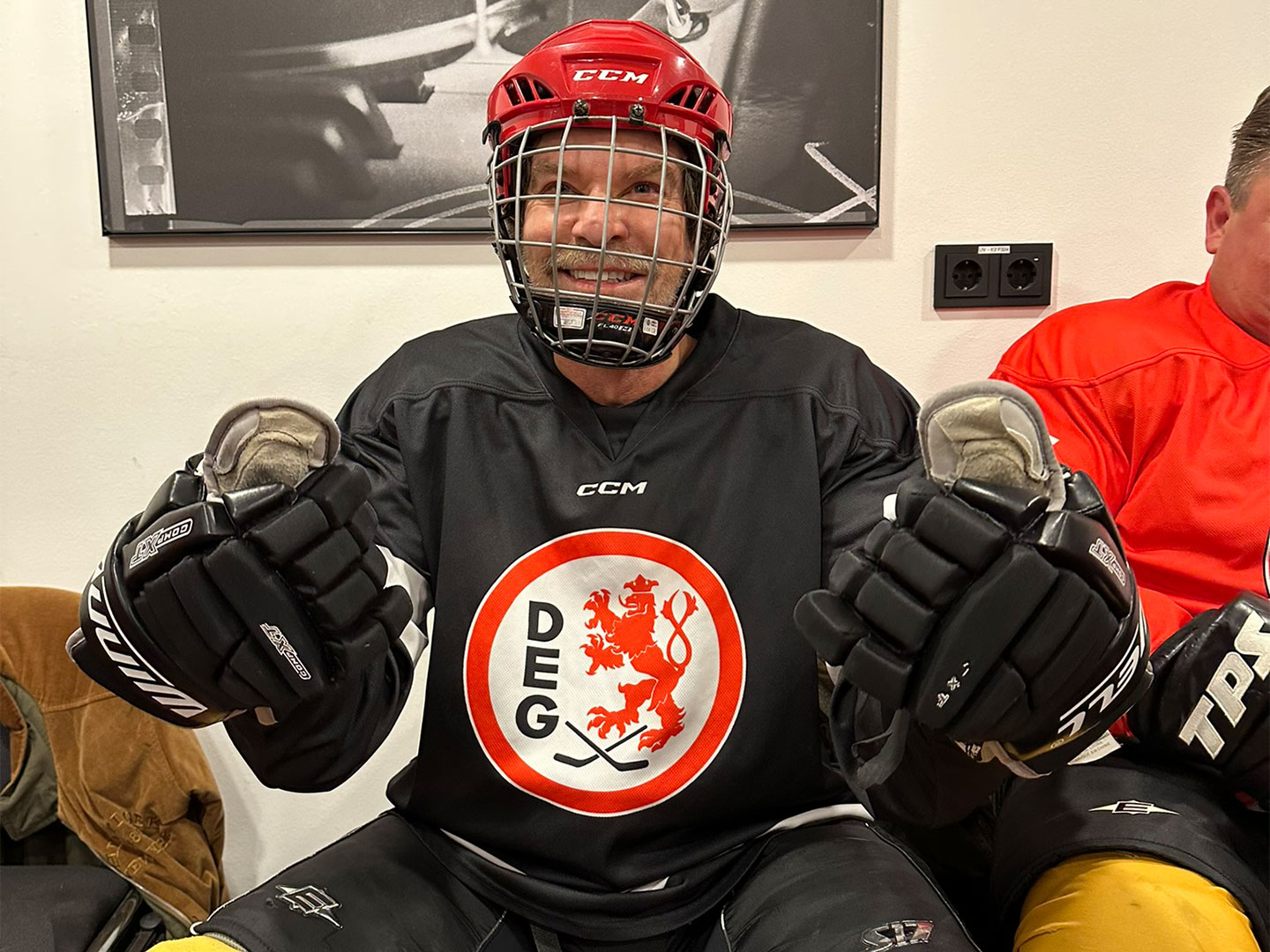 Person in Eishockeyausrüstung mit ein schwarzes Trikot sitzt in einer Umkleidekabine.