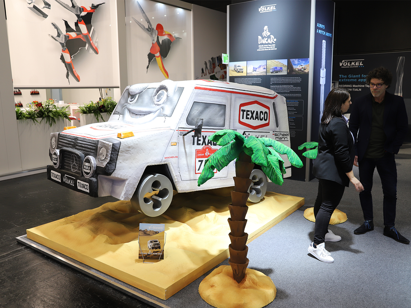 Modell eines Fahrzeugs mit TEXACO-Logo auf einer Messe, umgeben von künstlichen Palmen.