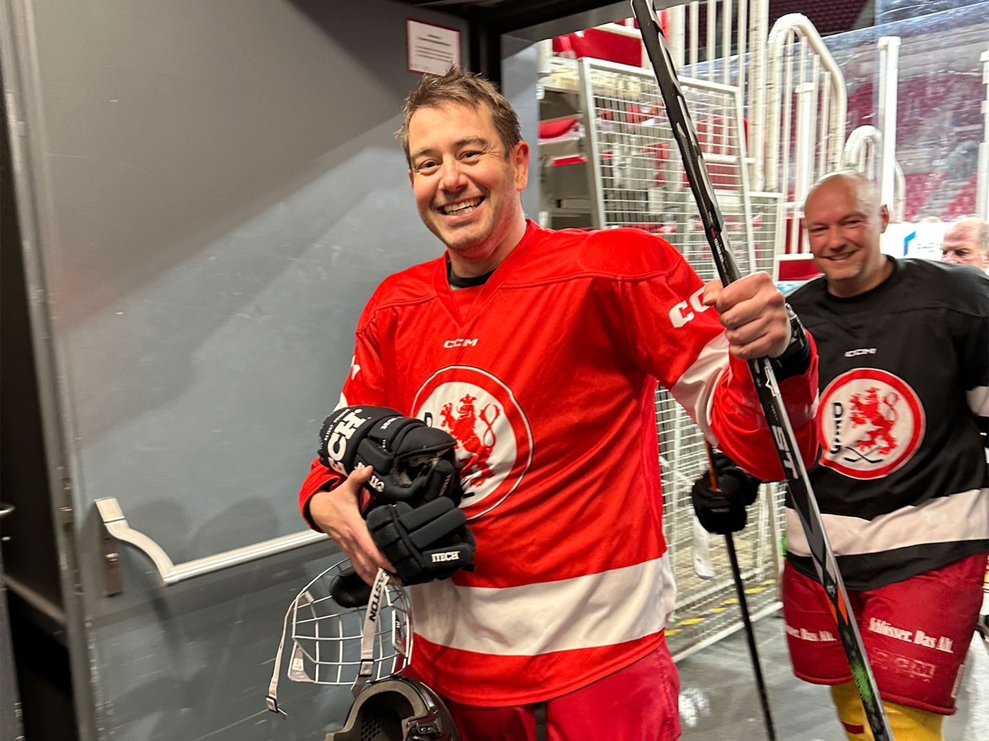 Zwei Teilnehmer gehen durch eine Tür. Der vordere trägt ein rotes Trikot, der hintere ein schwarzes.