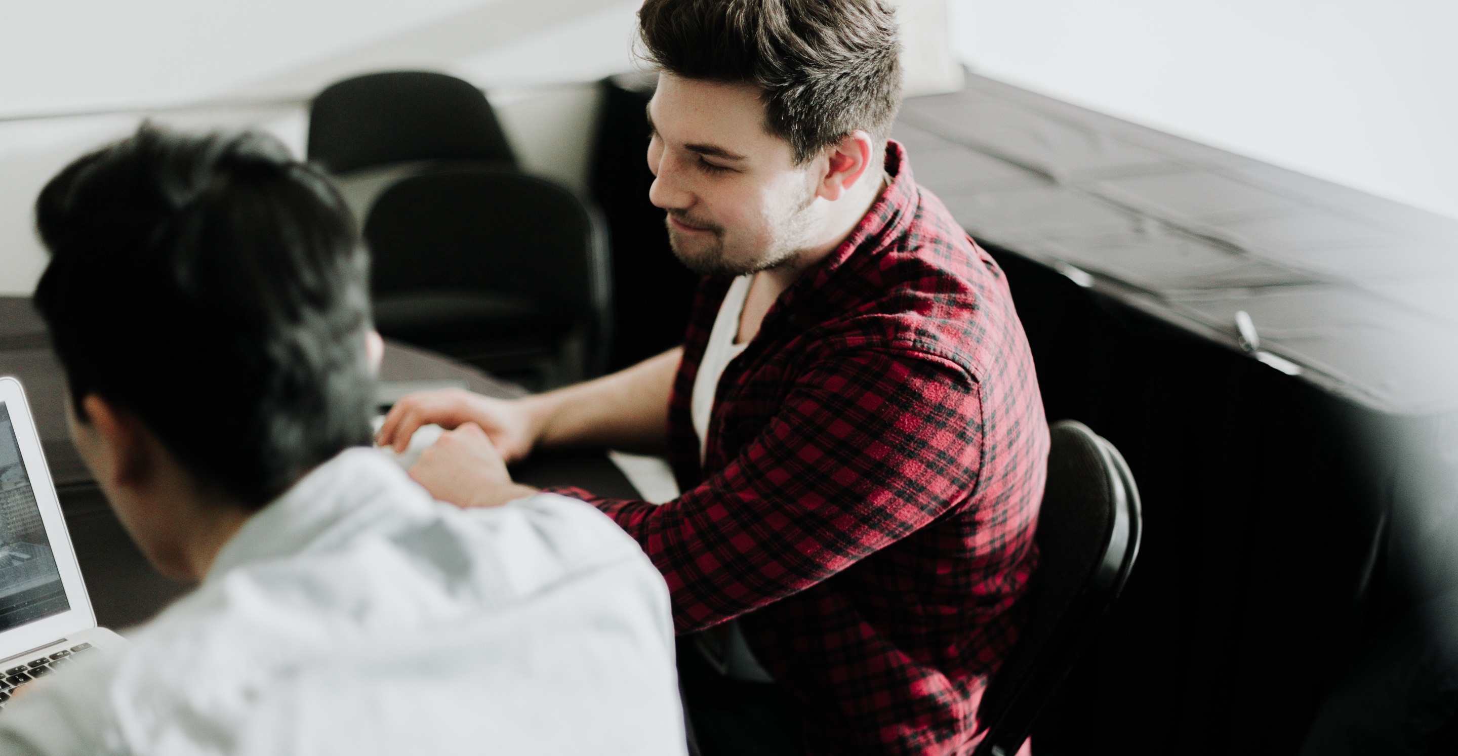 Dos individuos sentados en una mesa, uno con camisa a cuadros.