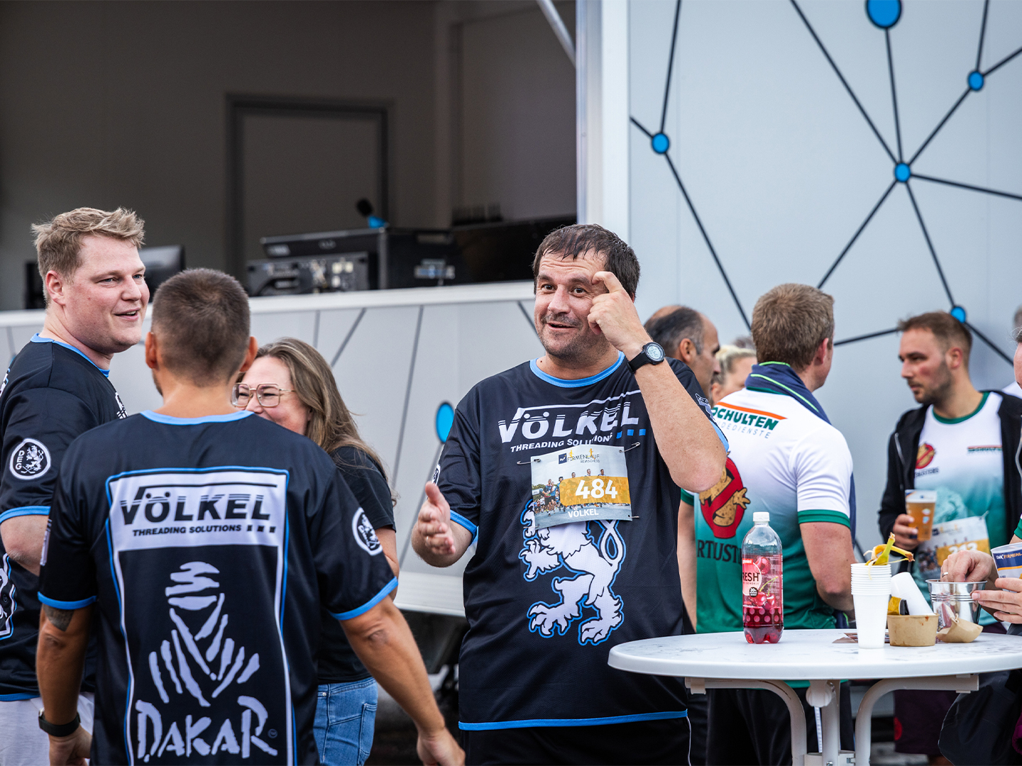 VÖLKEL-Team genießt Gespräche nach dem Lauf am Getränkestand. Keywords: Firmenlauf Remscheid, VÖLKEL, Team, Sportevent 2025