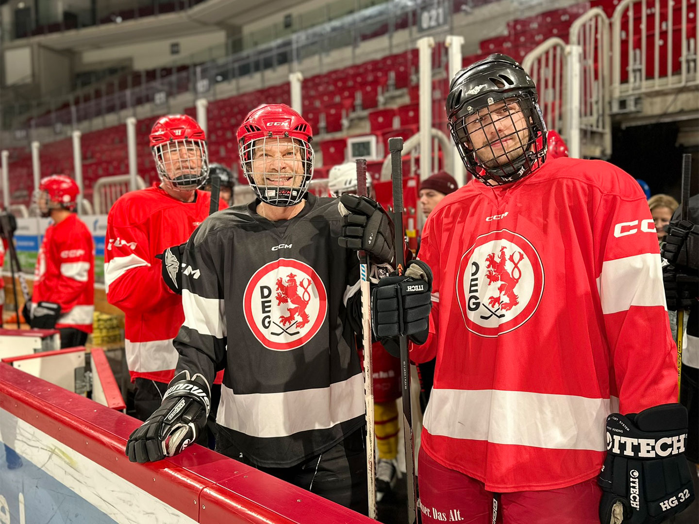 Eine Gruppe von Eishockeyspielern in roten und schwarzen DEG-Trikots steht am Spielfeldrand.