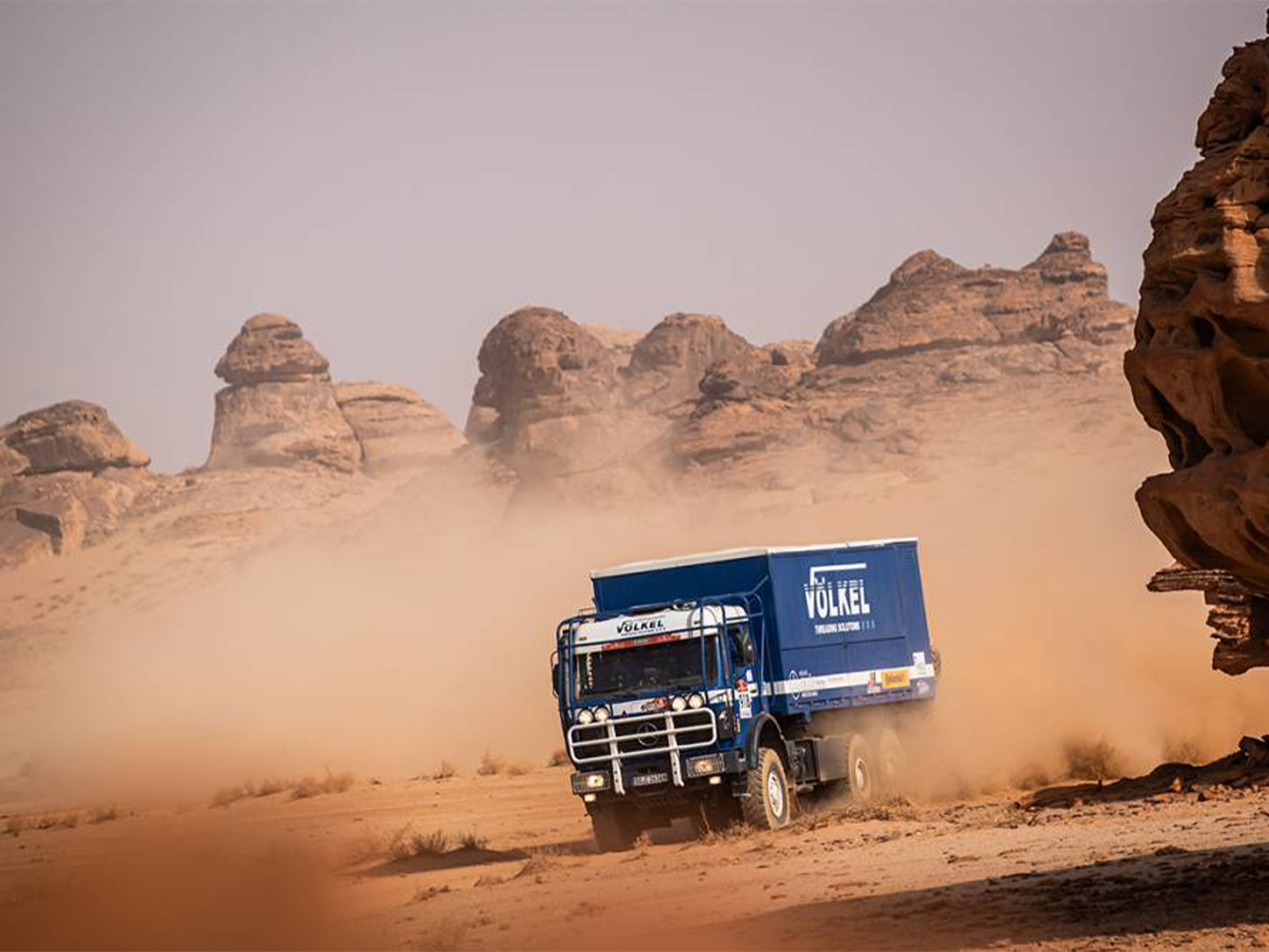 Rallyefahrzeug des Team VÖLKEL bei der Dakar Classic, auf der Wüstenpiste, vor markanter Felskulisse