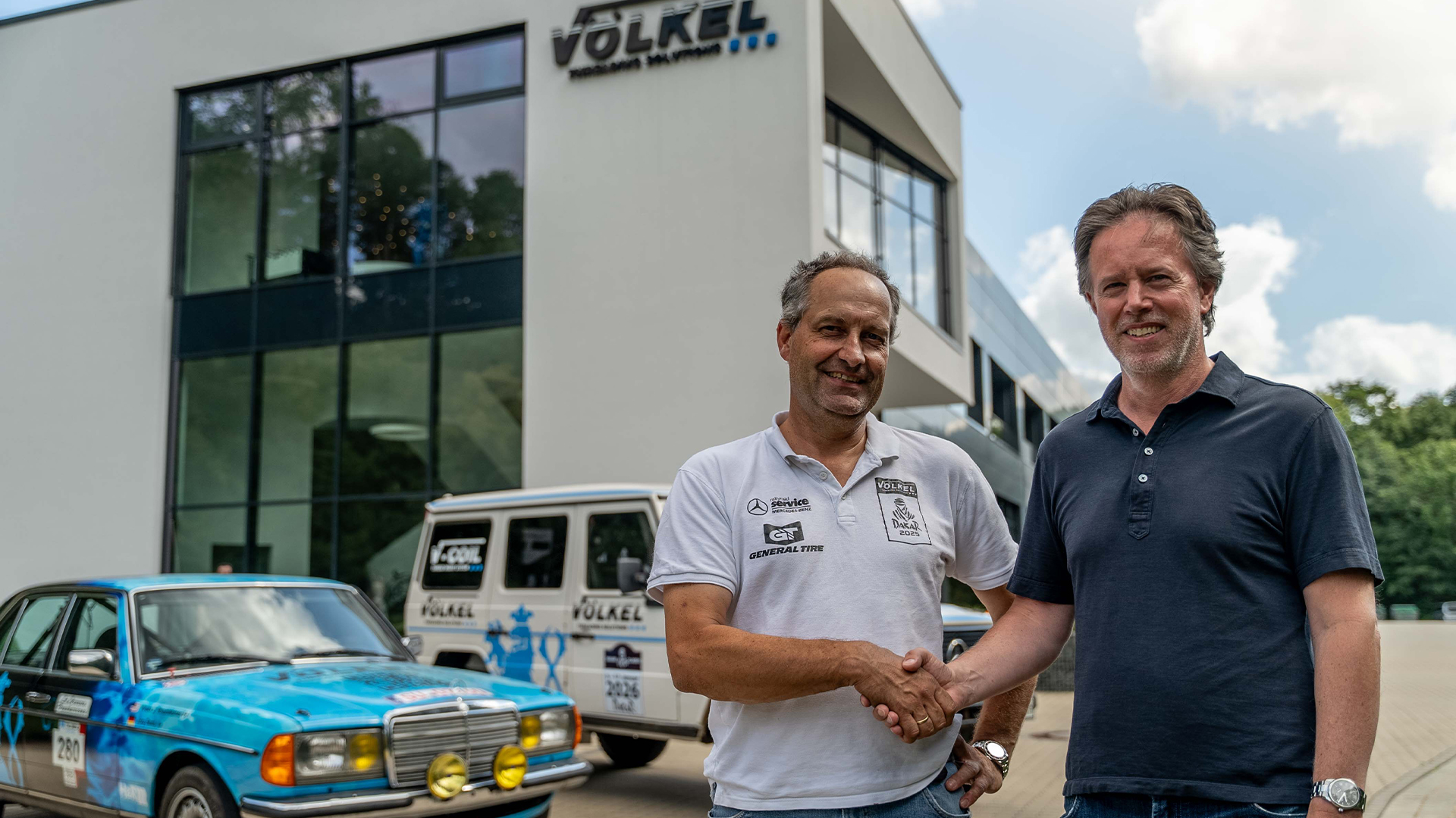 VÖLKEL investiert in Rally Raid Service Jörg Sand und Daniel Völkel vor dem VÖLKEL Gebäude mit Rallye-Fahrzeugen, Partnerschaft Rally Raid Service