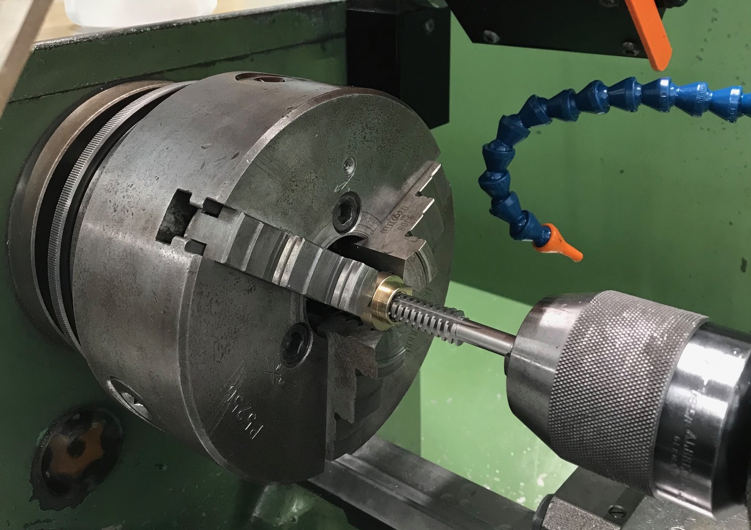 Detailansicht eines Maschinengewindebohrers, der ein Gewinde in ein Metallwerkstück in einer industriellen Drehmaschine schneidet.