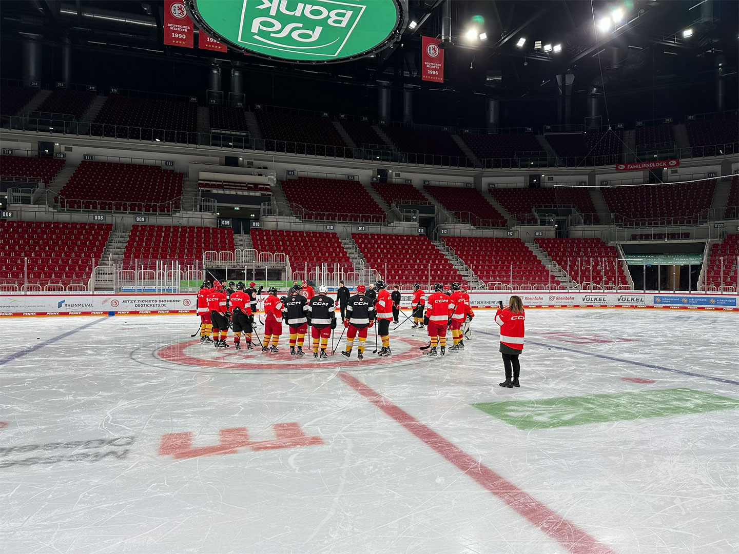 Eine Gruppe von Eishockeyspielern in roten und schwarzen Uniformen steht im Kreis auf dem Eis.