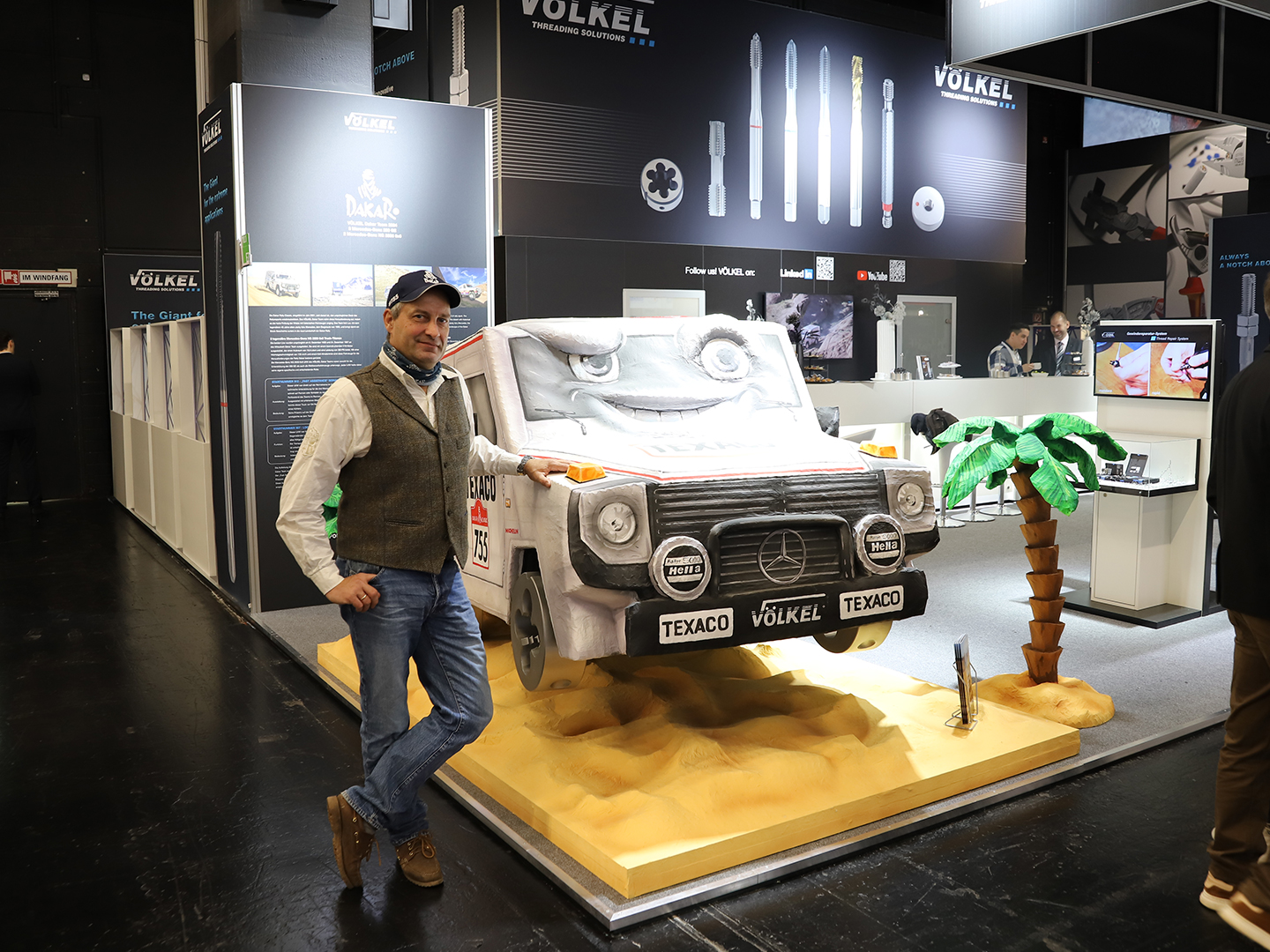 Jörg Sand posiert neben einem Modell eines Mercedes-Benz Fahrzeugs mit Texaco-Branding auf einer Messe.