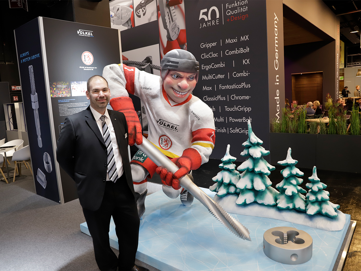 Person neben einer großen Statue eines Eishockeyspielers auf einem Ausstellungsstand der Marke VÖLKEL