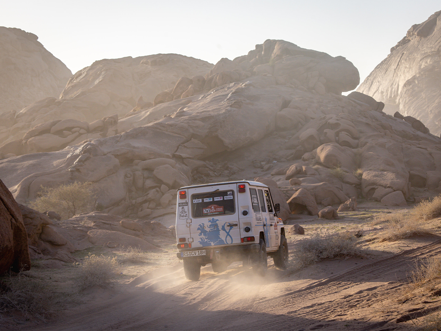 Rallyefahrzeug des Team VÖLKEL bei der Dakar Classic, auf steiniger Bergpiste, mit aufgewirbelter Staubfahne