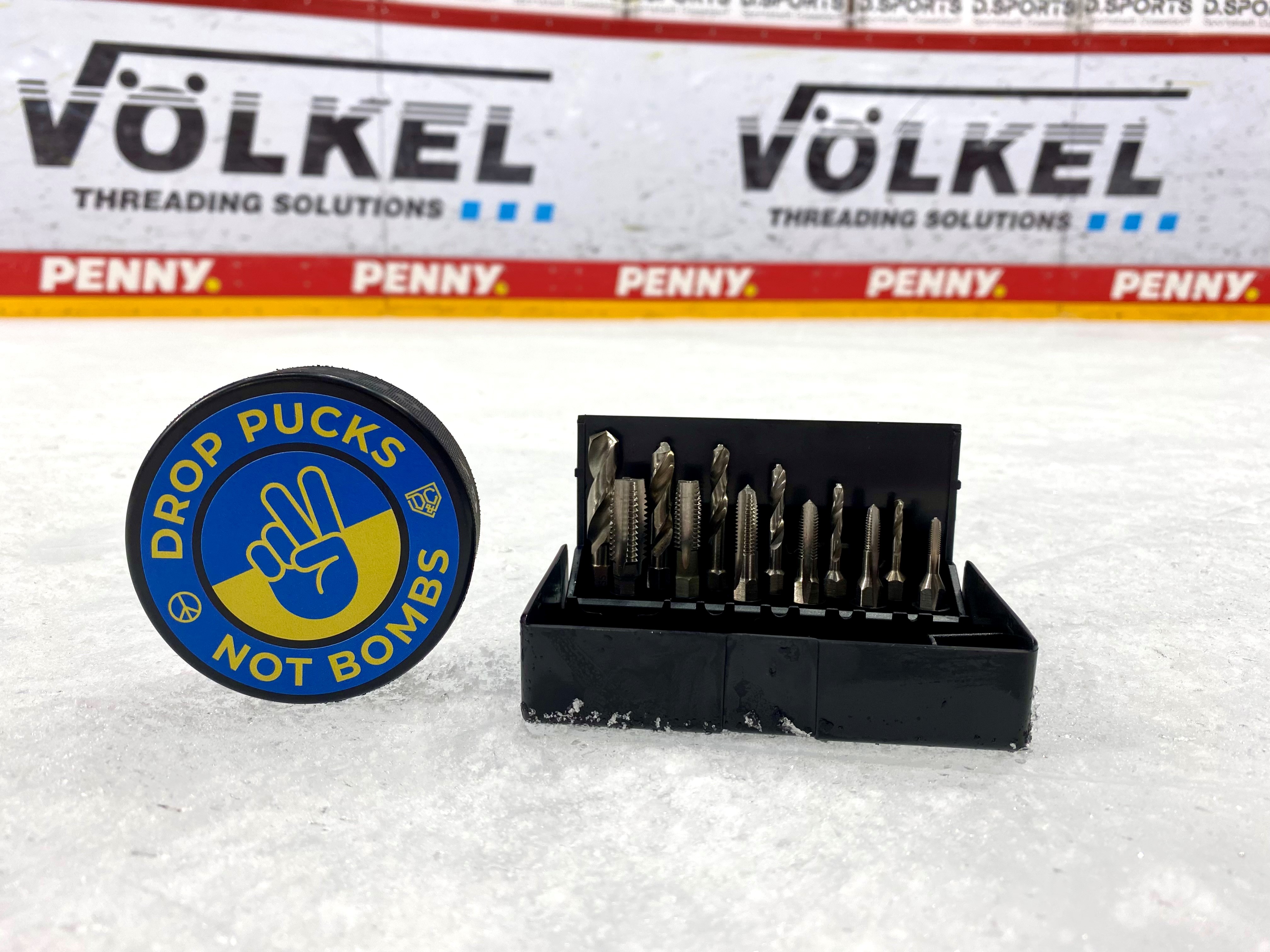 Eishockey-Puck mit „Drop Pucks Not Bombs“-Aufdruck in ukrainischen Farben neben einem VÖLKEL Gewindebohrer-Set