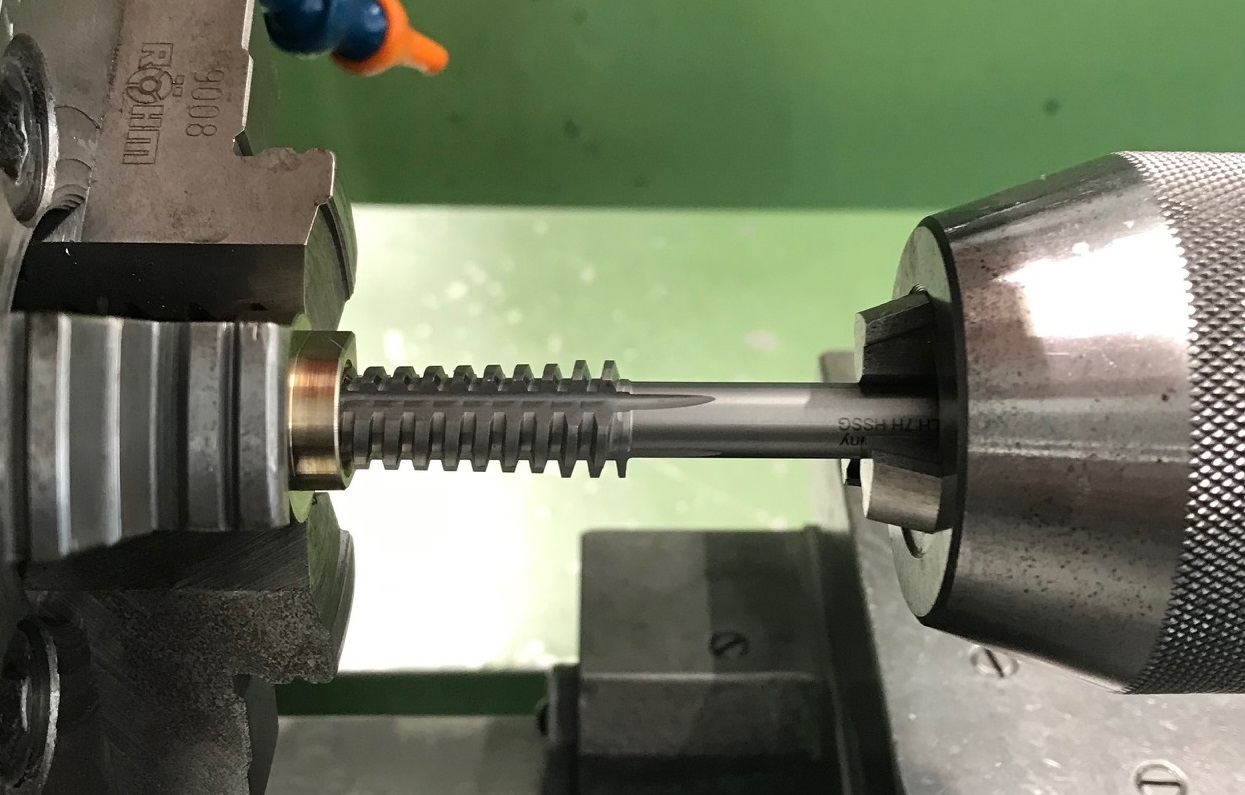 Maschinengewindebohrer schneidet präzise Gewinde in ein Metallstück in einer Drehmaschine.