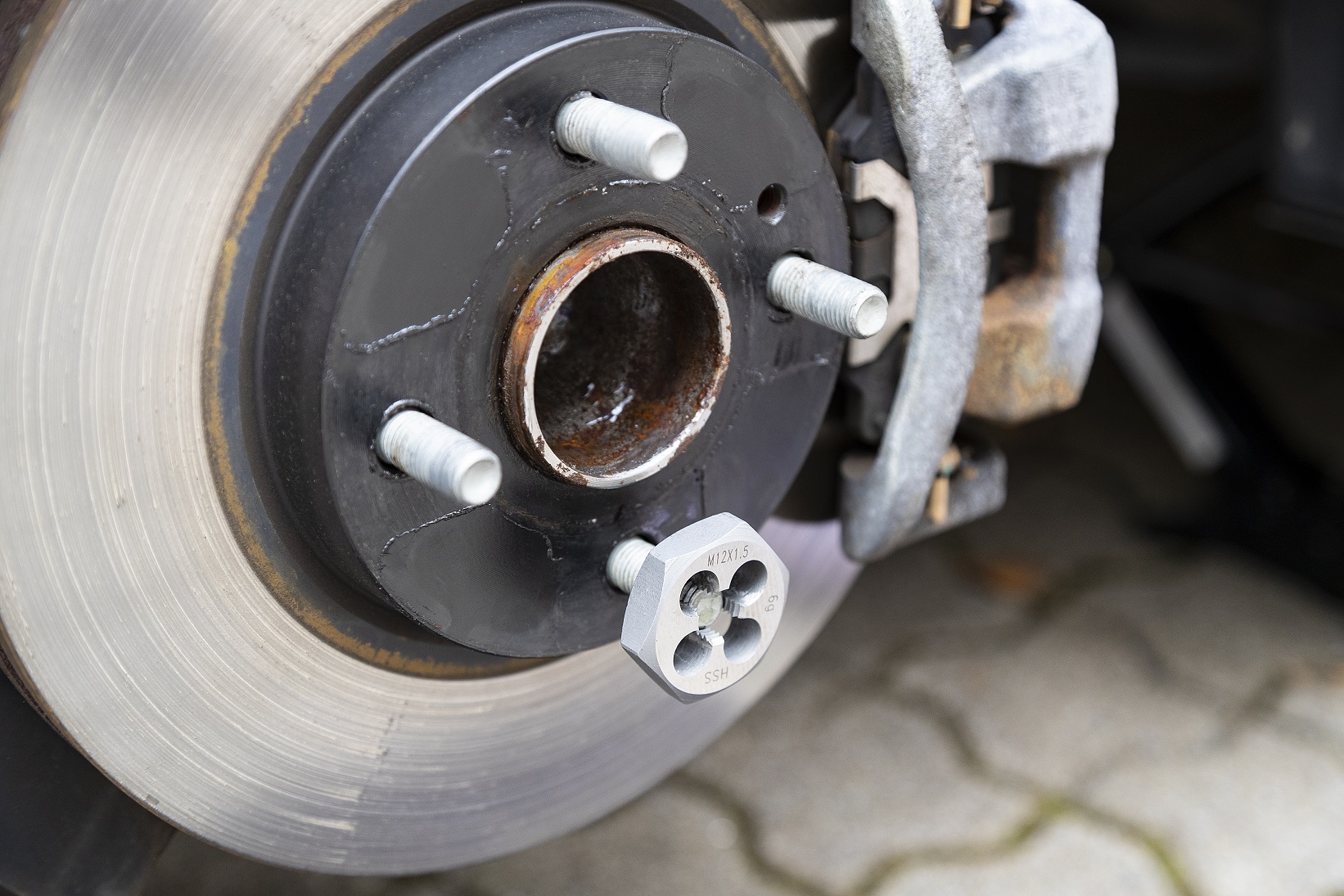Wheel stud thread recut M12x1.5 Recutting M12x1.5 wheel stud thread using HSS die, close-up of brake disc and hub.