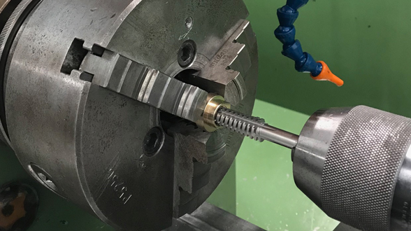 Industrielles Gewindeschneiden eines Metallzylinders mit einem Maschinengewindebohrer und Spannfutter.