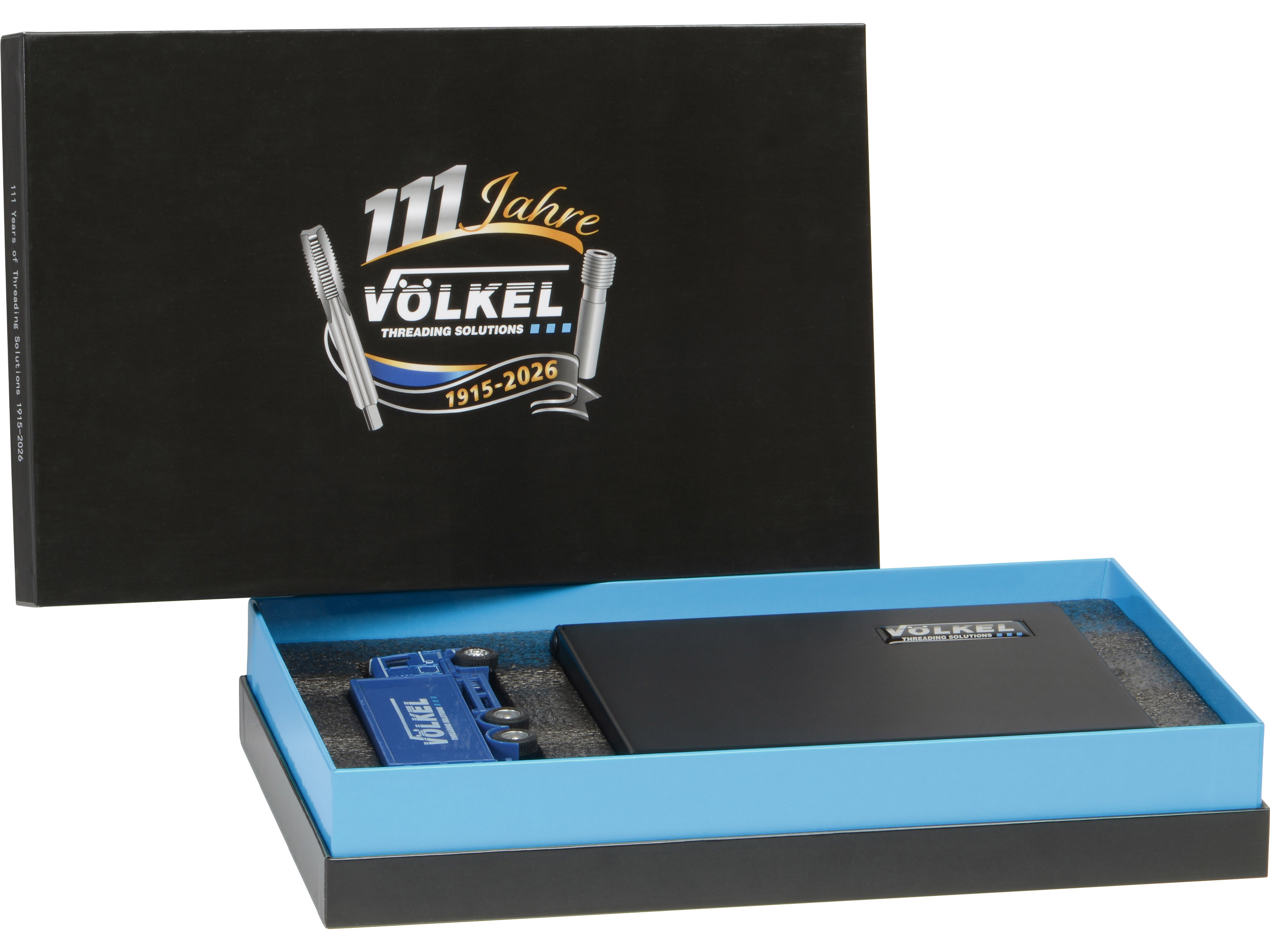 Geöffnete VÖLKEL Jubiläumsbox mit schwarzer Bit-Box und blauem LKW-Modell im Schaumstoff-Inlay.