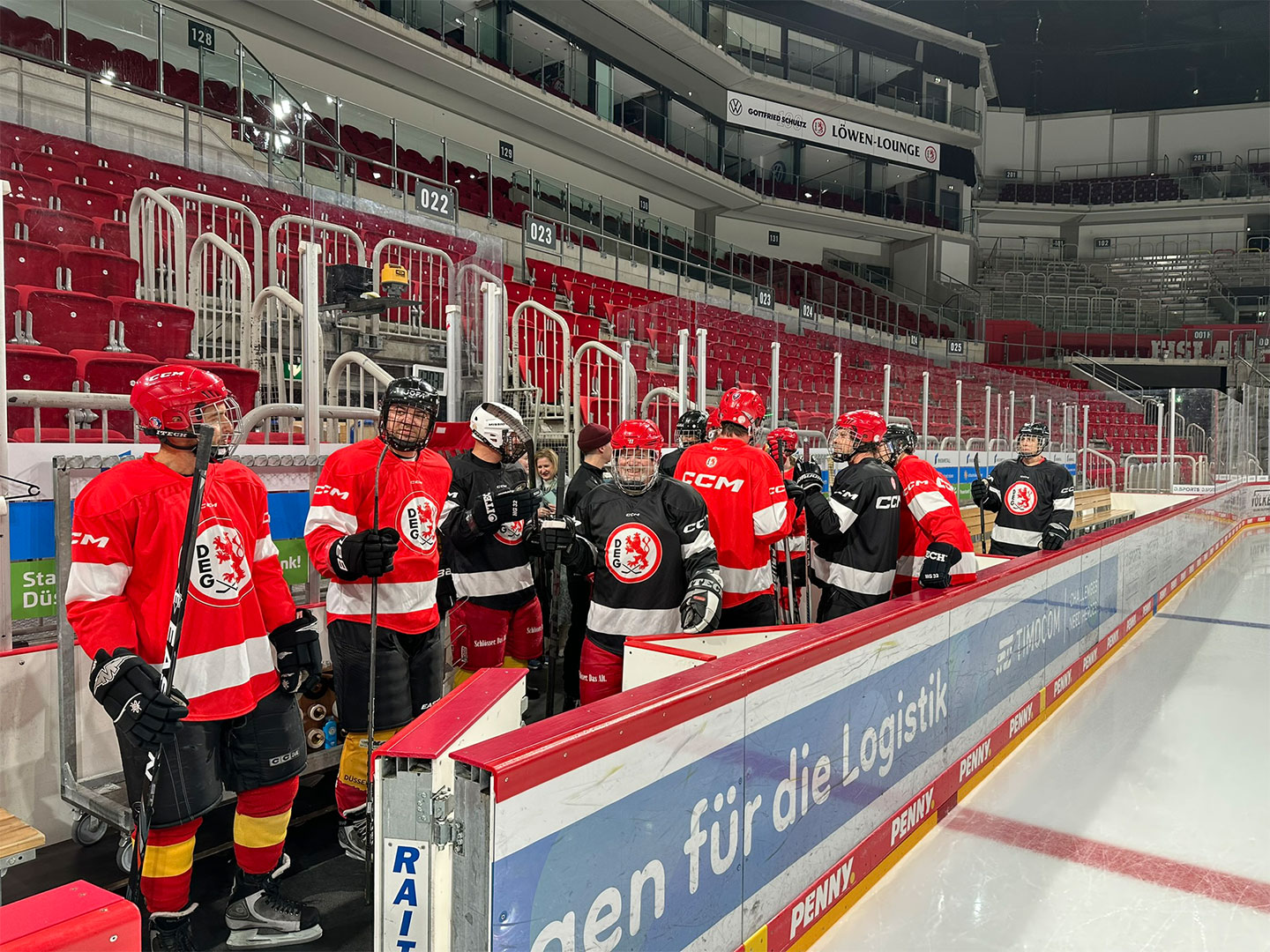 Eine Gruppe von Eishockeyspielern in roten und schwarzen Uniformen steht am Spielfeldrand.