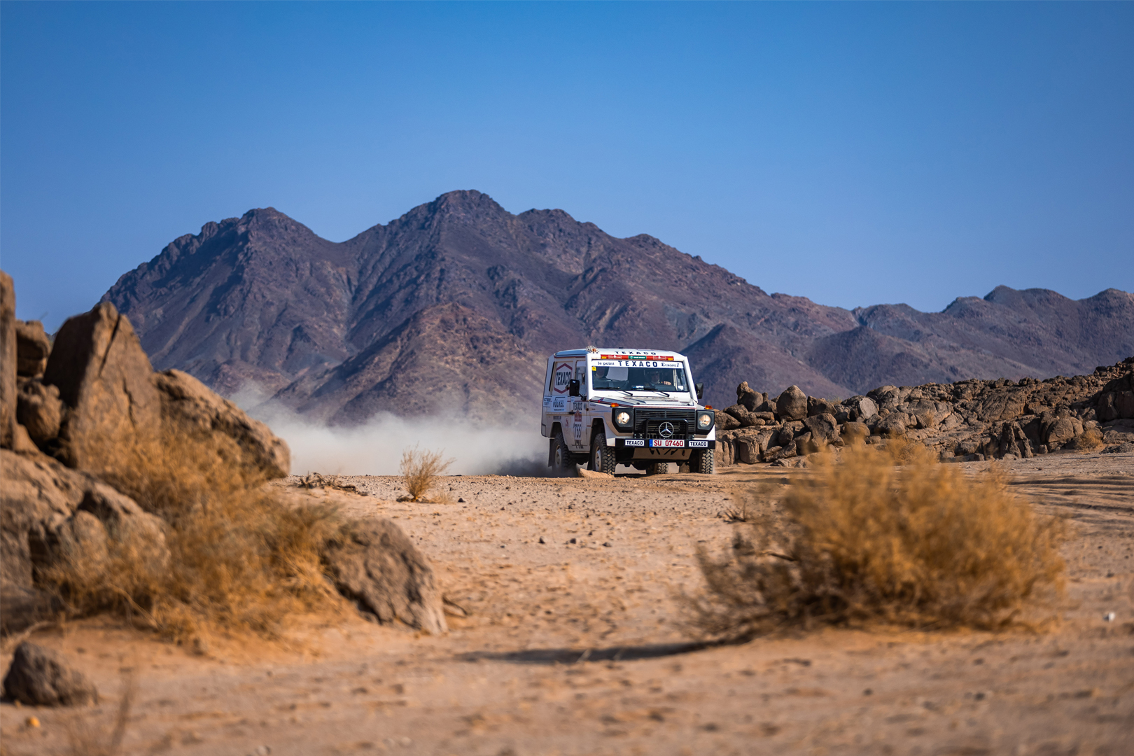 Voiture de rallye avec pneus Michelin et logo VÖLKEL franchissant le sable.