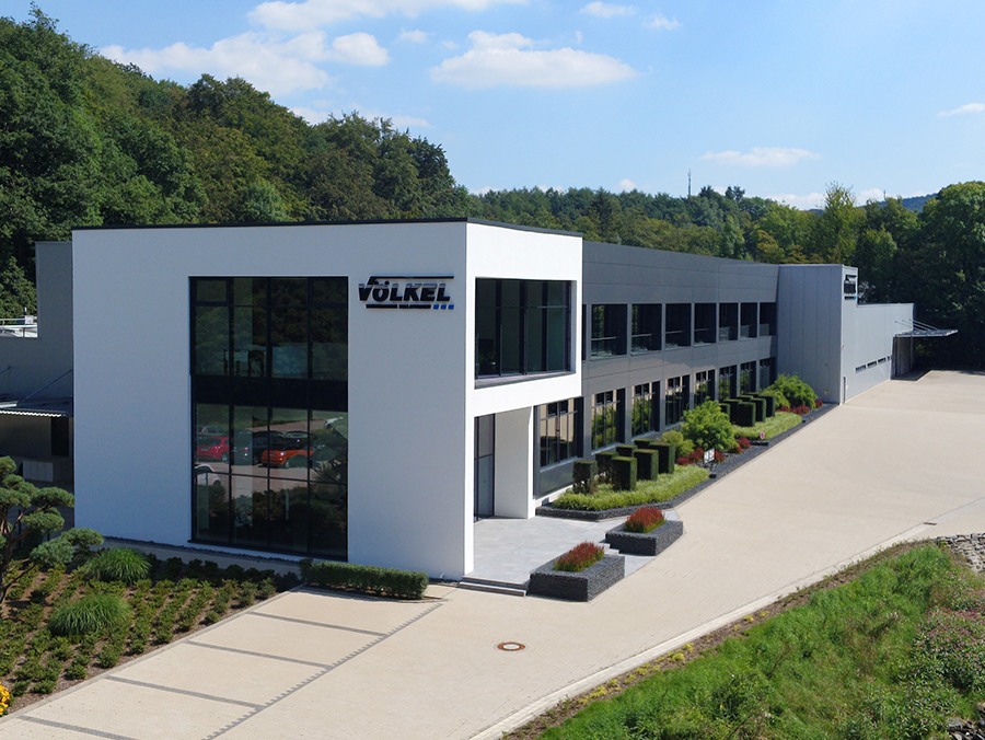 Bâtiment principal de Völkel GmbH avec façade en verre et nature.
