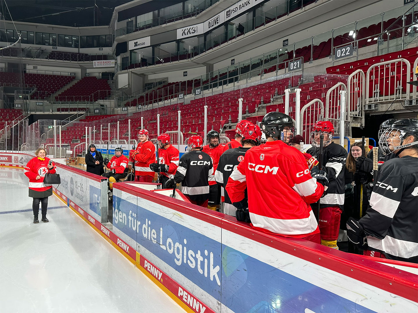 Eine Gruppe von Eishockeyspielern in roten und schwarzen Uniformen steht nahe der Bank.