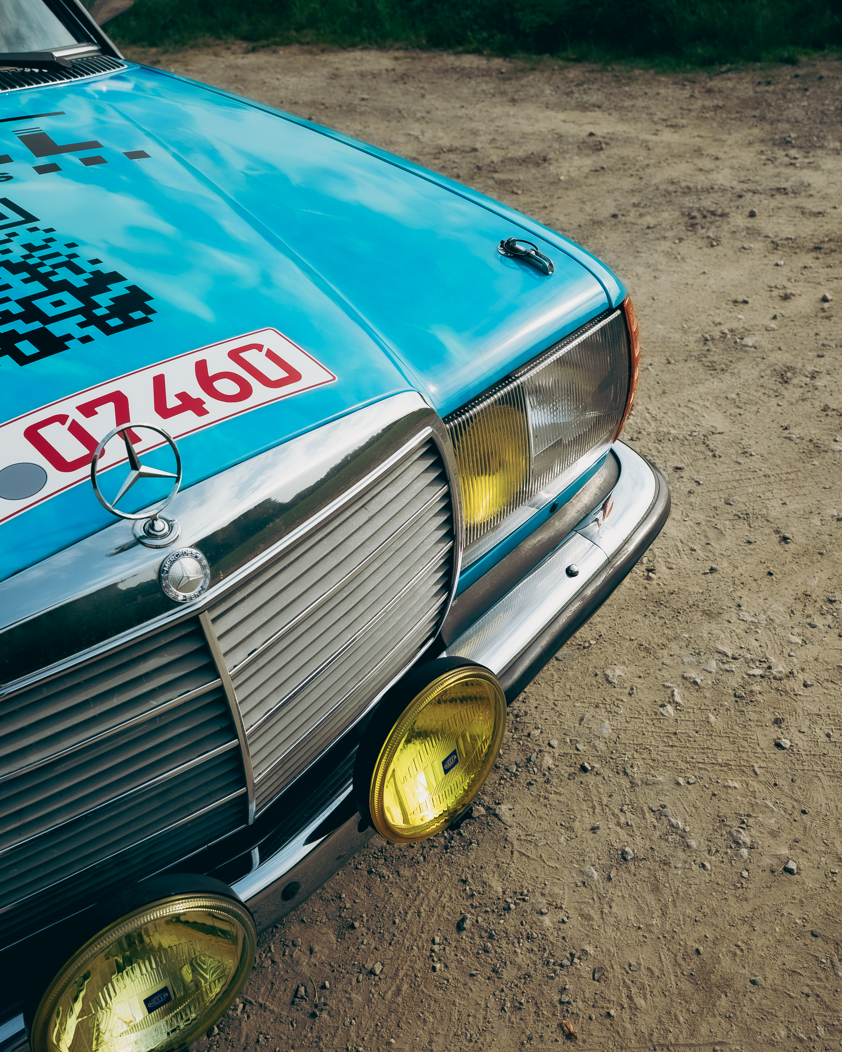 Mercedes-Benz 280E W123 Rallye Frontscheinwerfer Frontansicht des Mercedes-Benz 280E W123 mit gelben Zusatzscheinwerfern, Rallye-Ausrüstung und Mercedes-Stern.