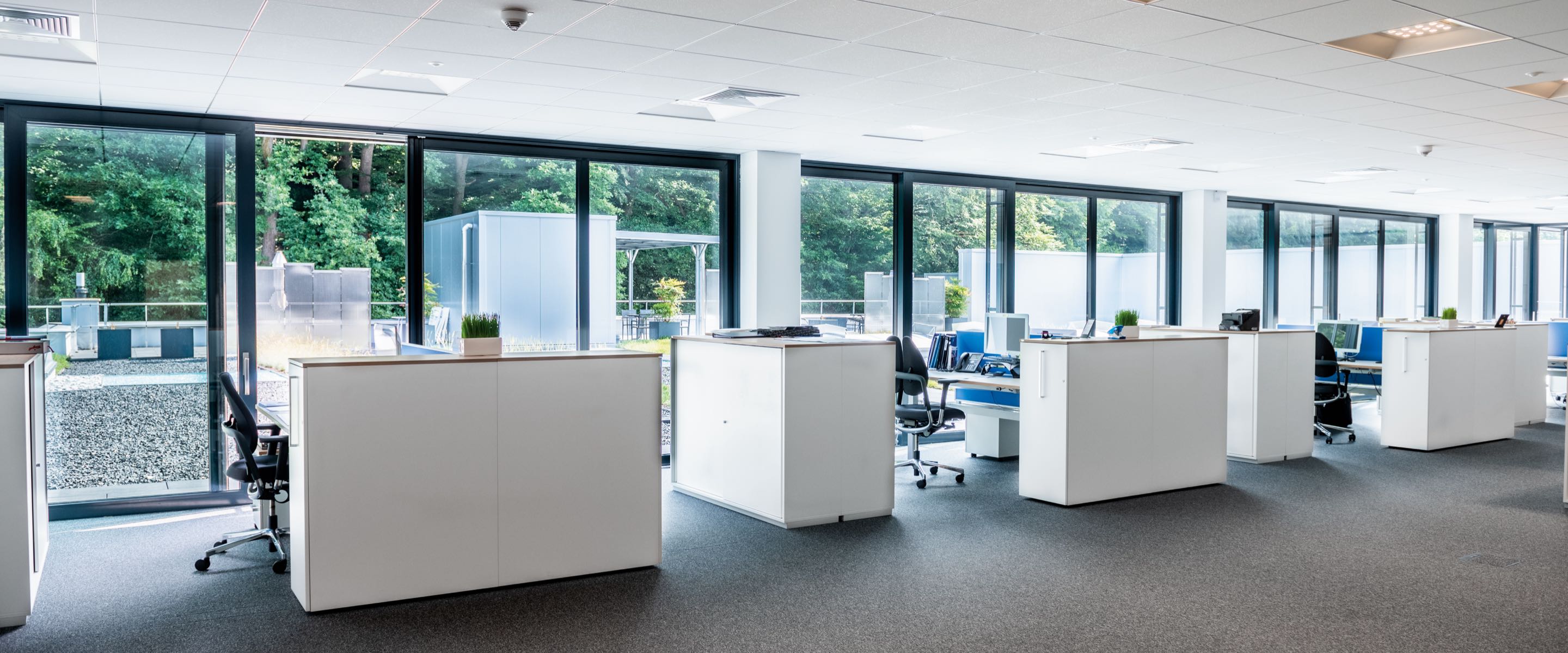 Moderner Büroraum mit weißen Schreibtischen und großen Fenstern.