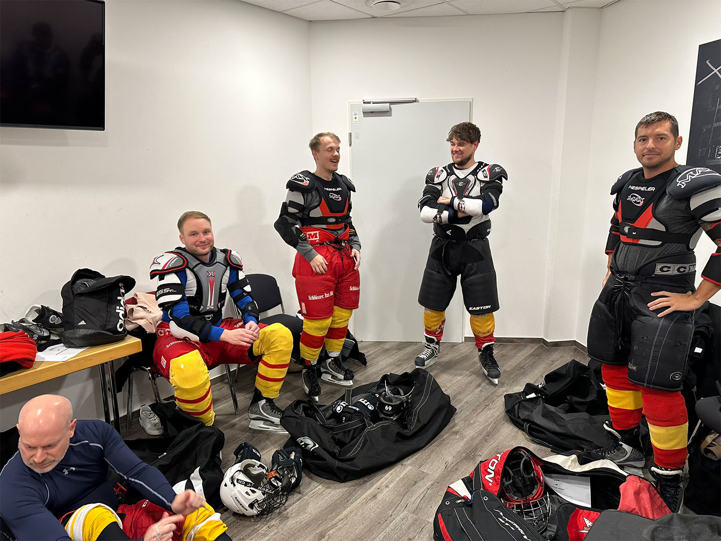 Vier Personen in einer Umkleidekabine tragen Eishockeyausrüstung und bereiten sich auf Hockey Day vor