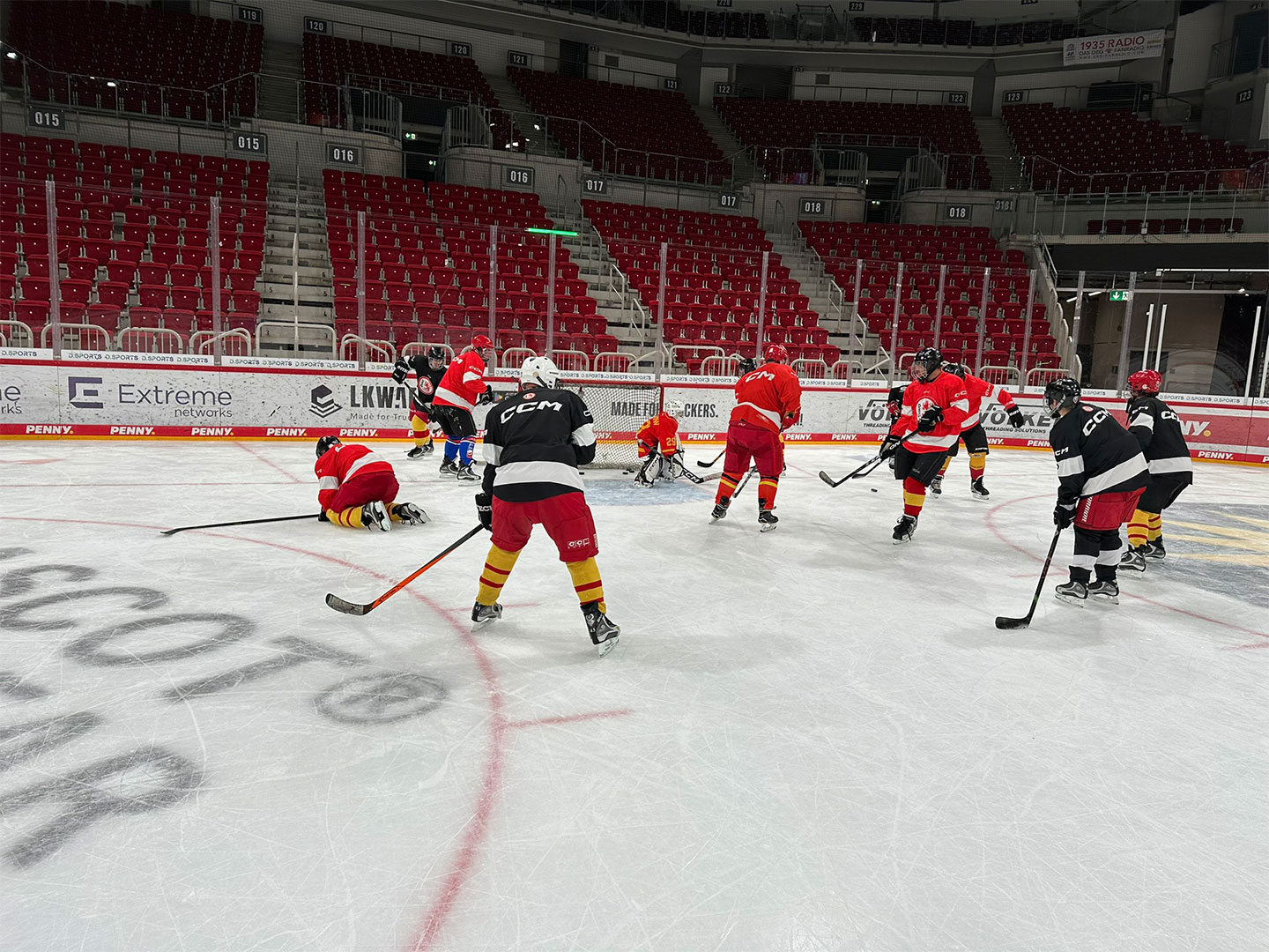 Eishockeyspieler in roten und schwarzen Trikots auf dem Eis.