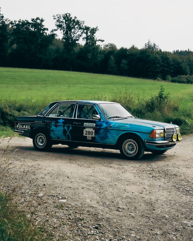Mercedes-Benz 280E W123 AMG del equipo VÖLKEL con el dorsal 280 frente a un prado